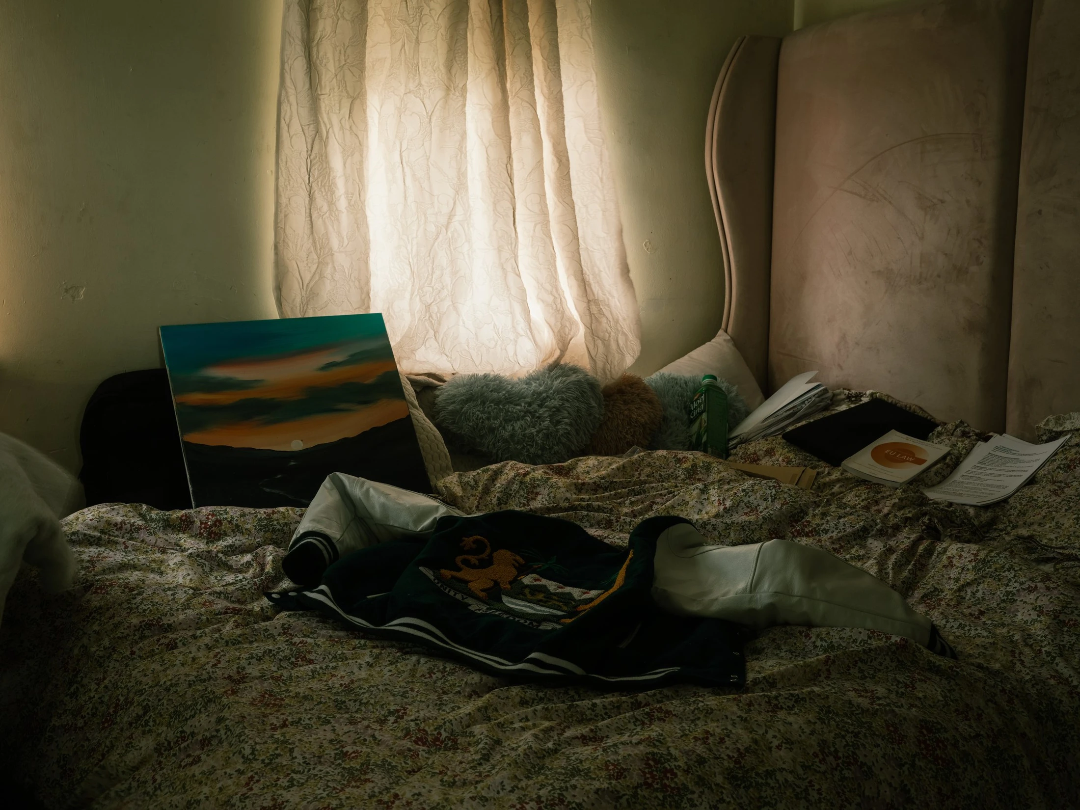 Abdulai’s room with books and clothes on a bed beside a curtained window