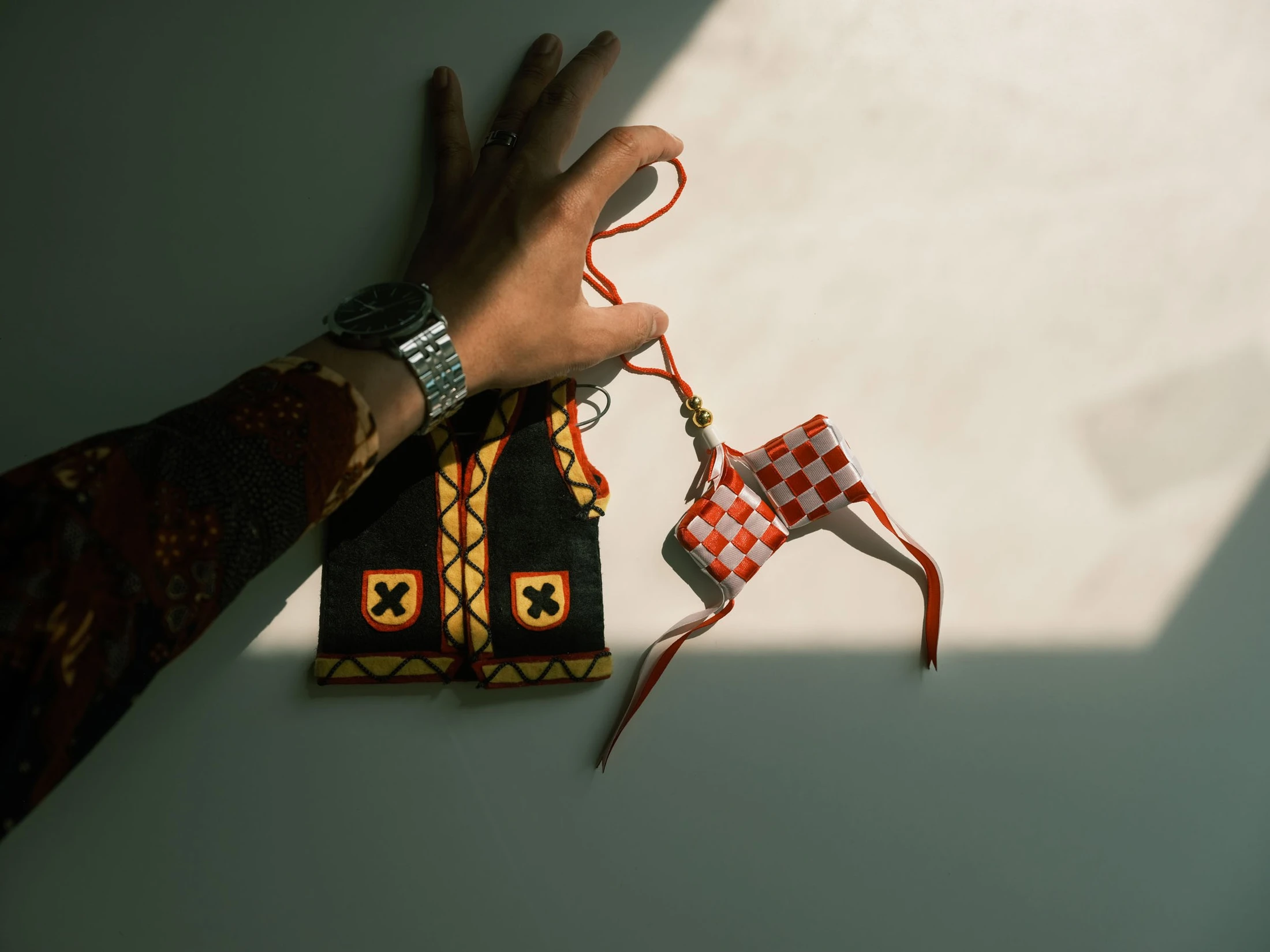 A hand raised into sunlight beside colourful hanging fabric