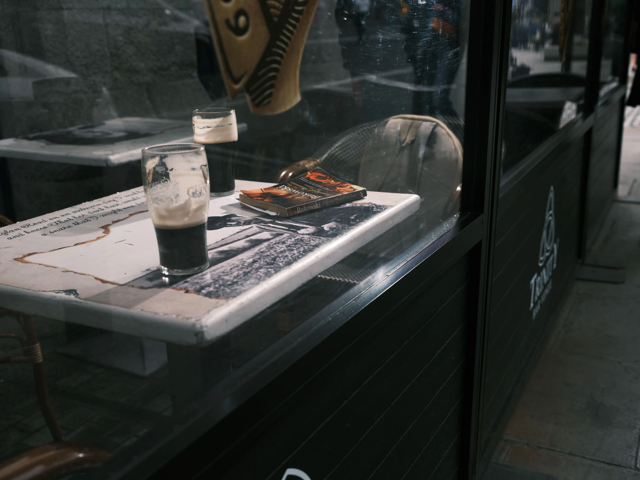 A pub table by a window with books, a glass and a cup