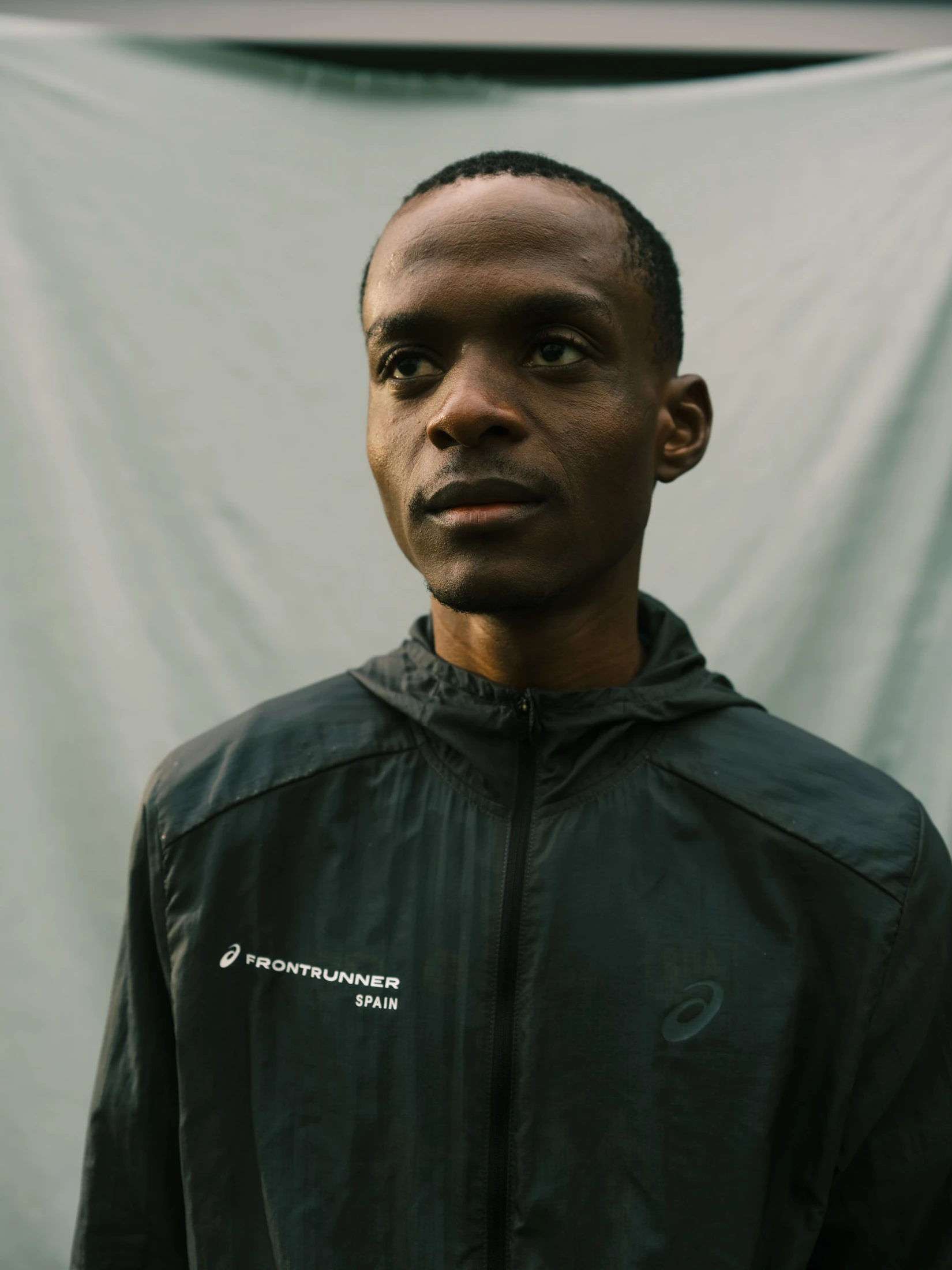 Portrait of Kahumburuka wearing a dark rain jacket against pale fabric