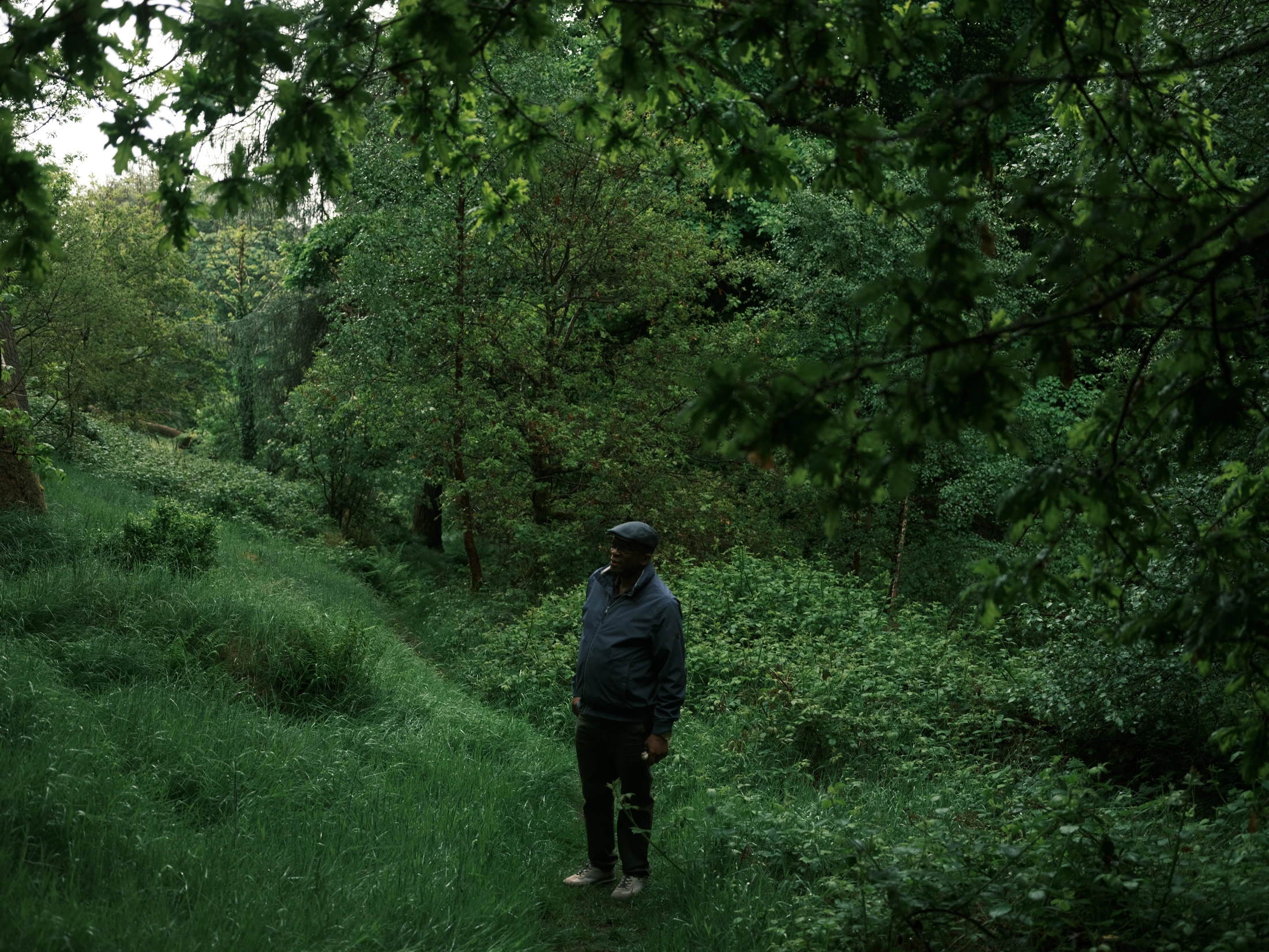 Lucky Khambule in a leafy wooded glen, wearing a cap