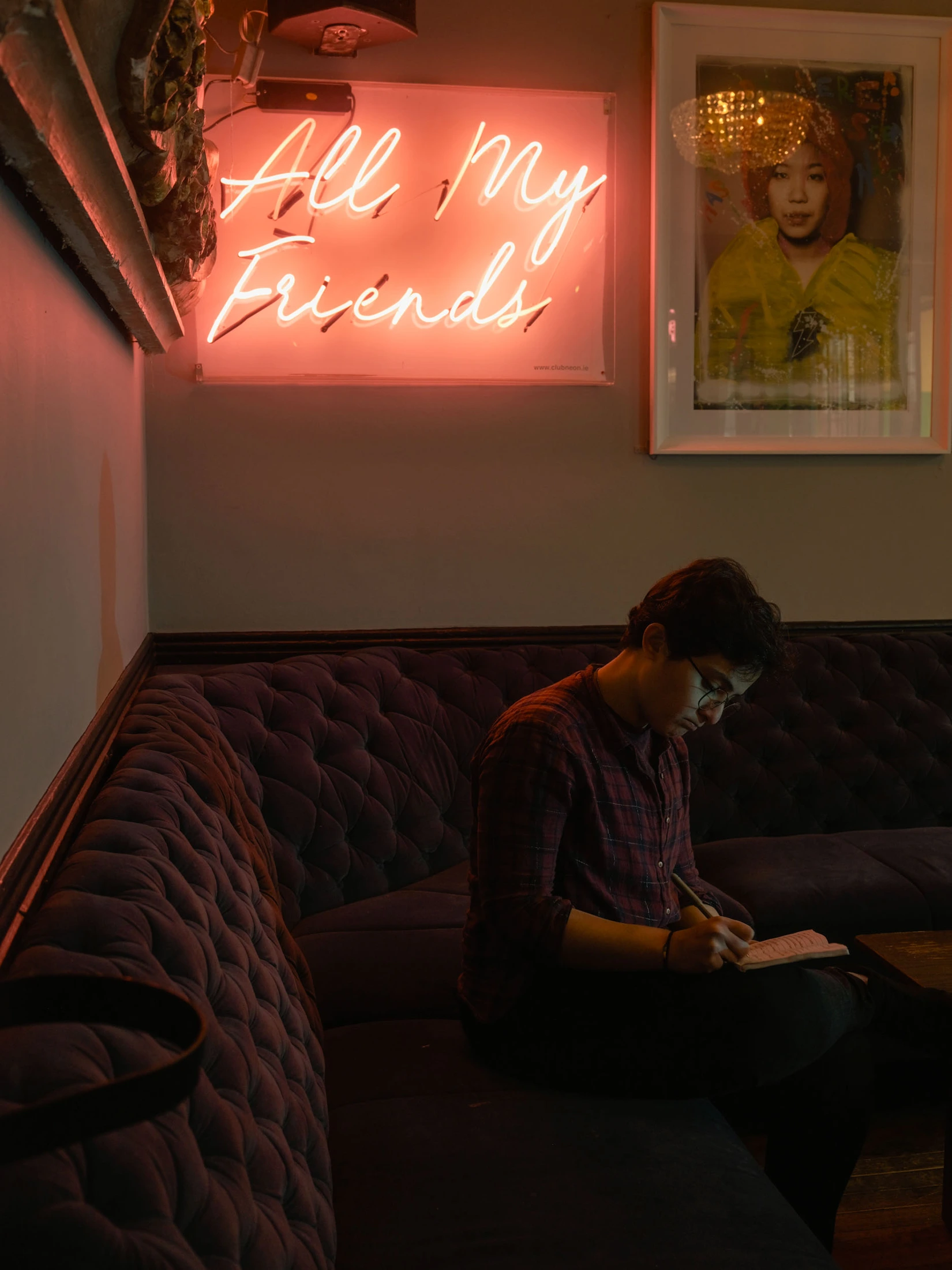 Levant writing in a notebook beneath a red neon sign