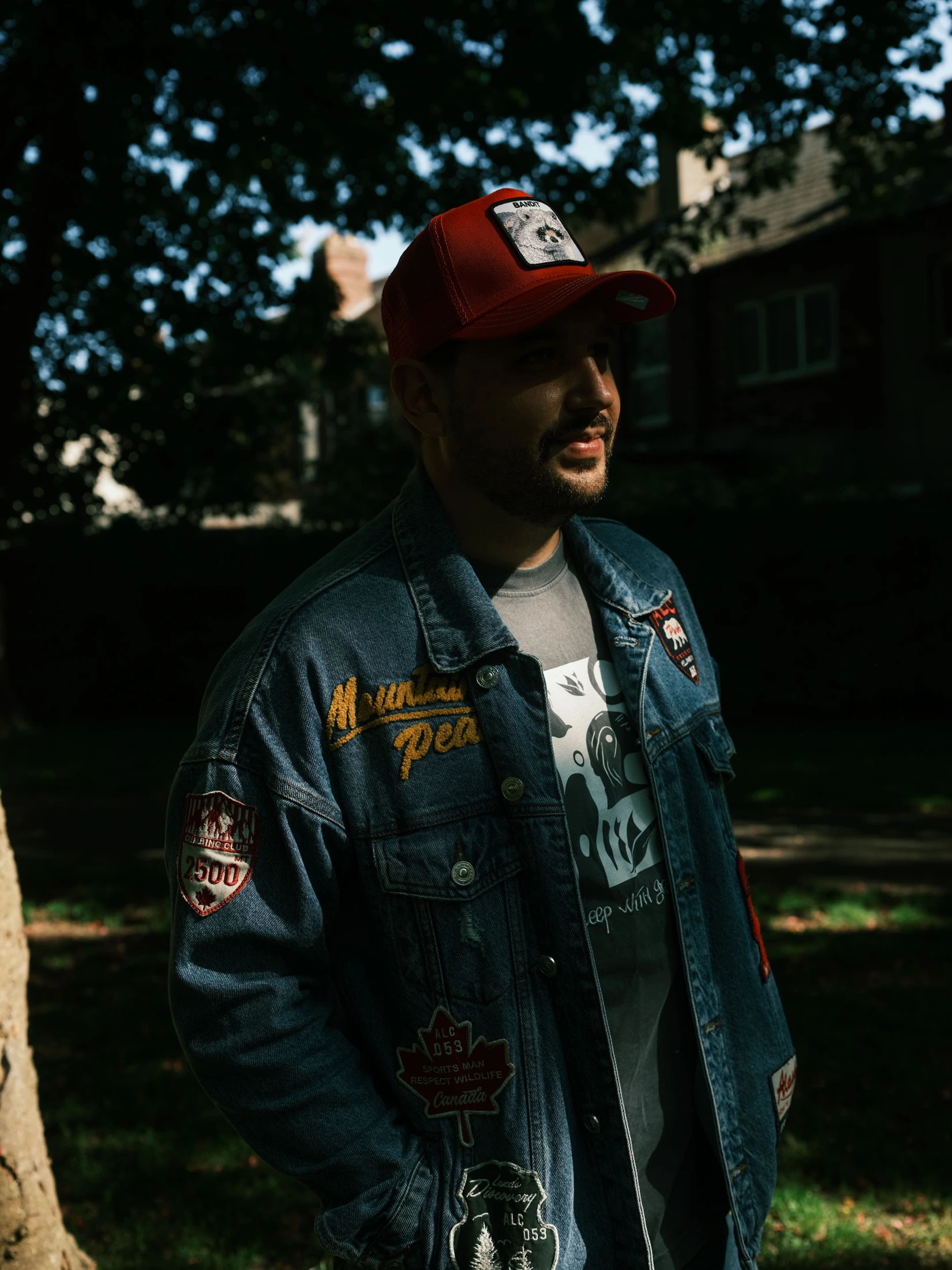 Portrait of Mykhailo wearing a red cap and denim jacket in a leafy park