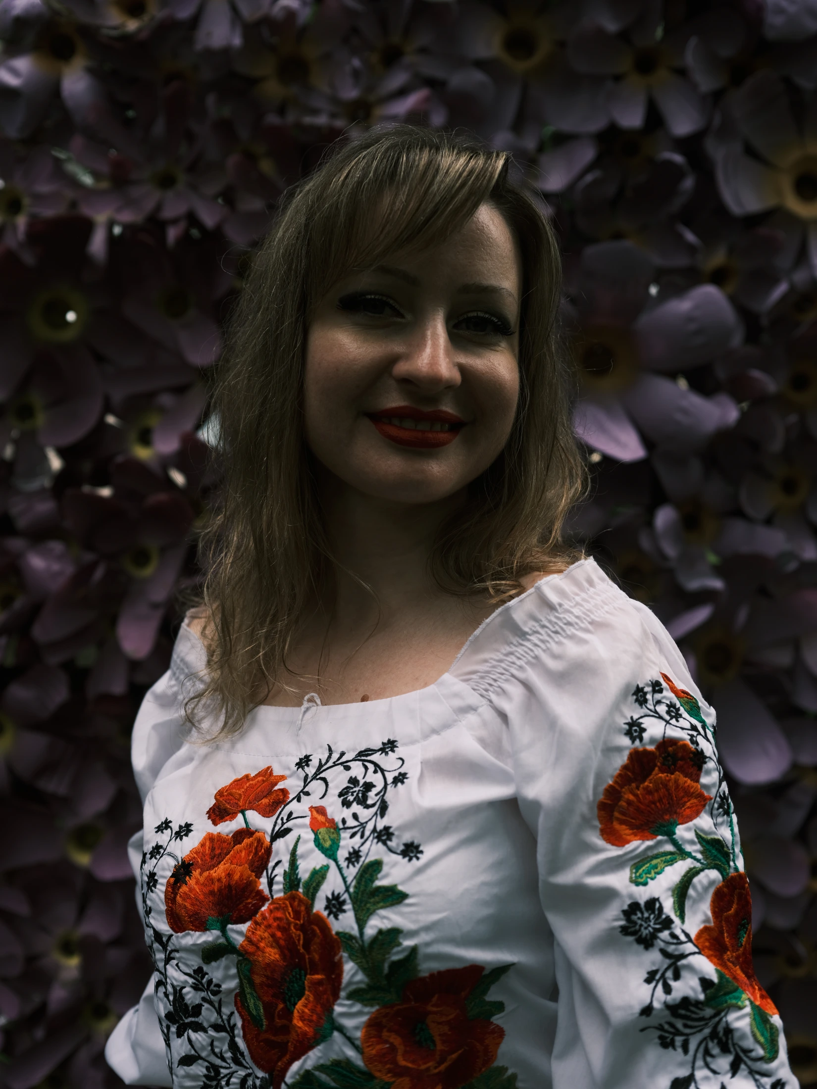 Olessia in an embroidered white blouse beside purple foliage