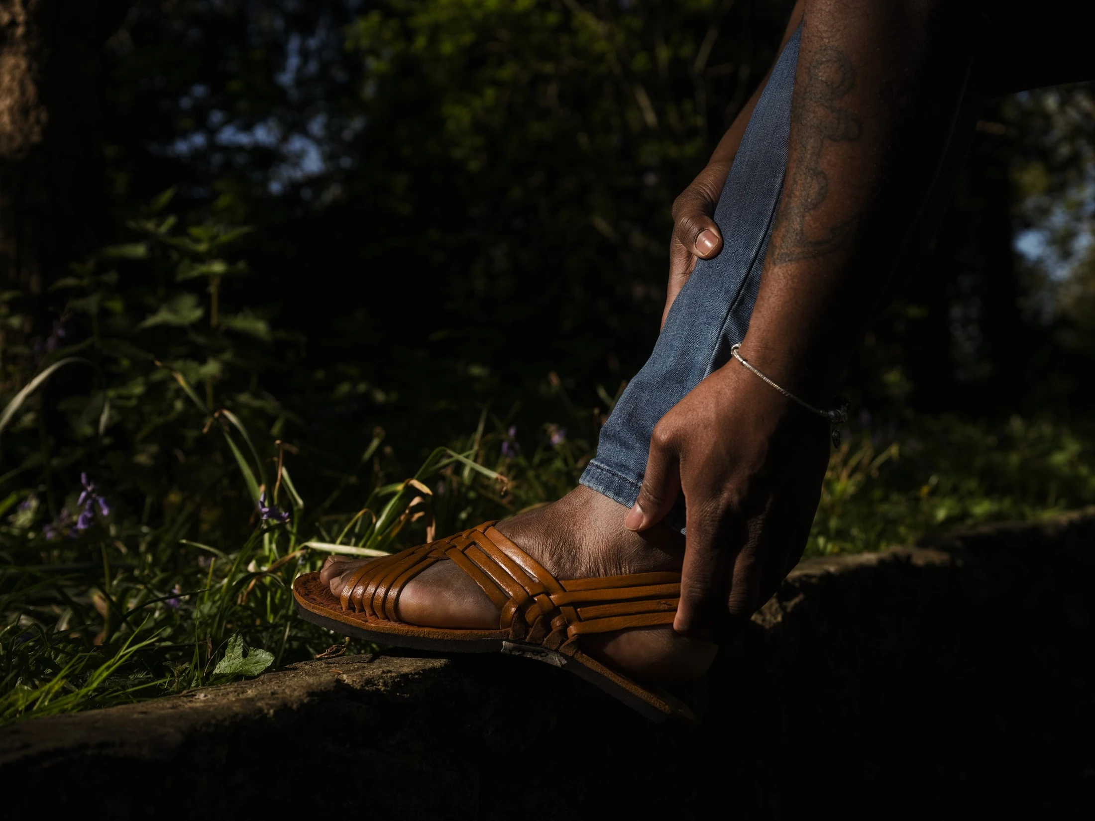A hand resting beside a polished brown shoe and small flowers