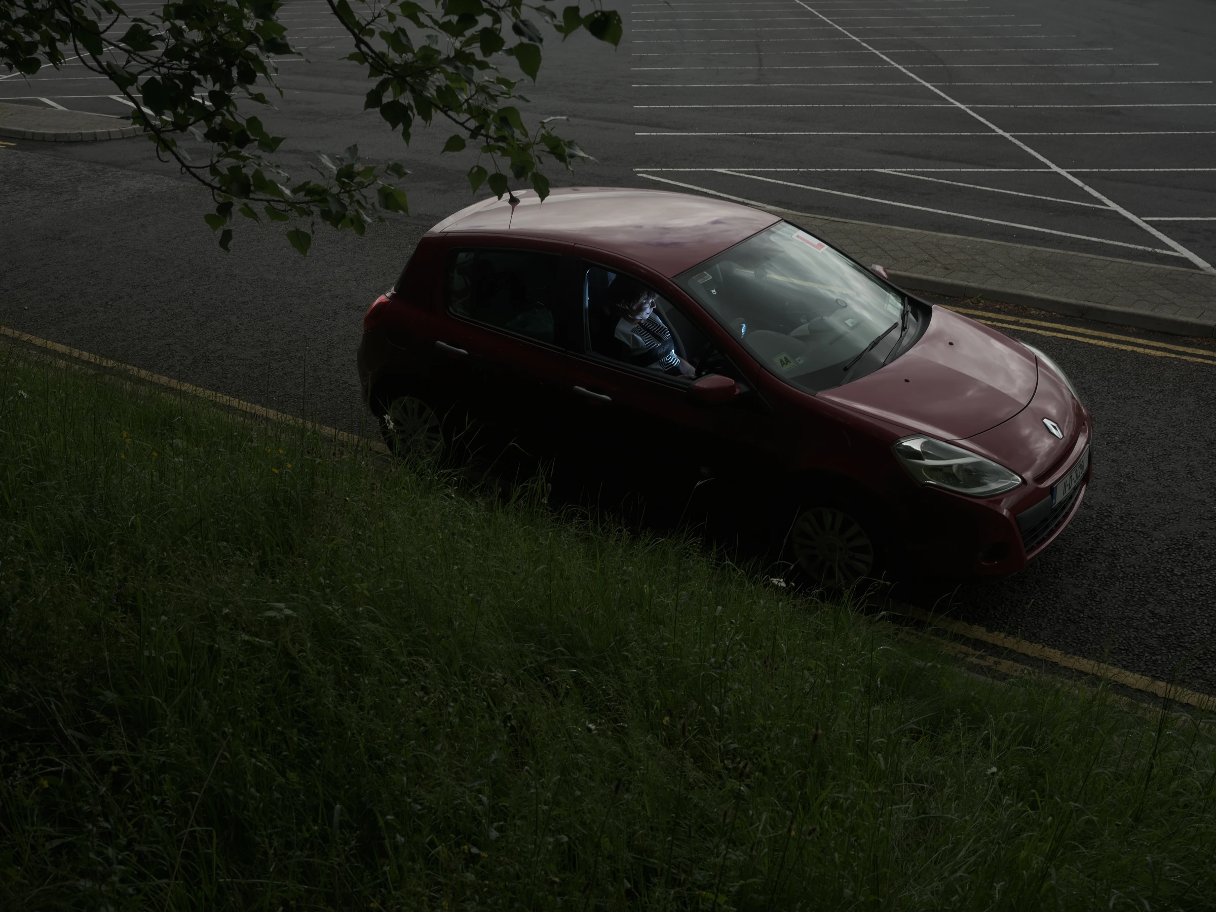 Rita sitting in a red car beside an empty car park