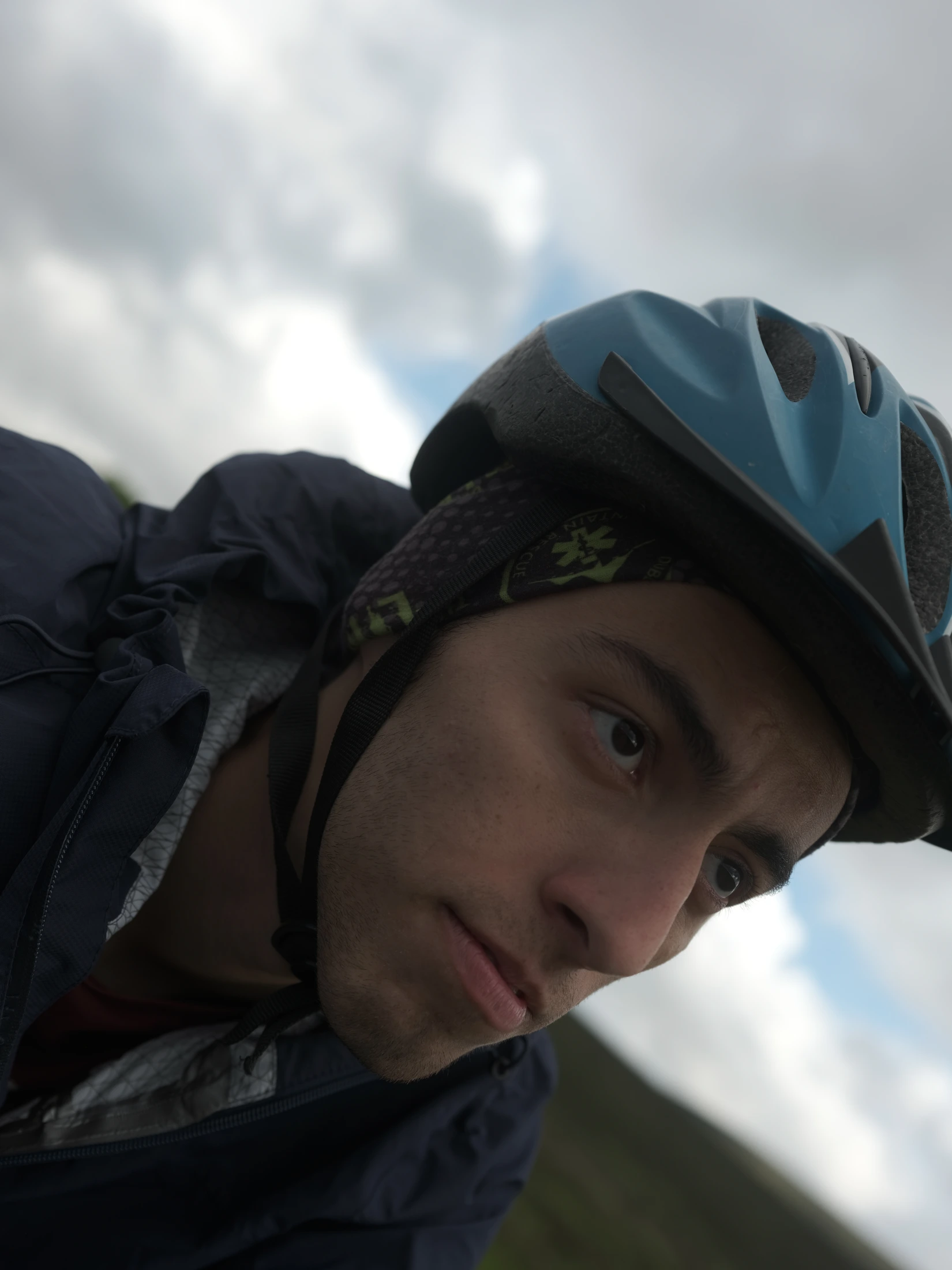 Close portrait of Siavash wearing a bicycle helmet under a cloudy sky